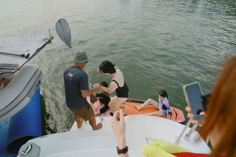 Multiple fishing rods extend over the side of a boat as people enjoy a day of deep sea fishing.