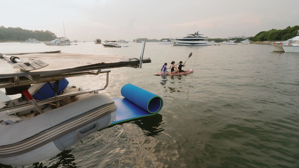 Panoramic view of boats anchored in a tranquil bay with green coastline and calm waters at sunset.