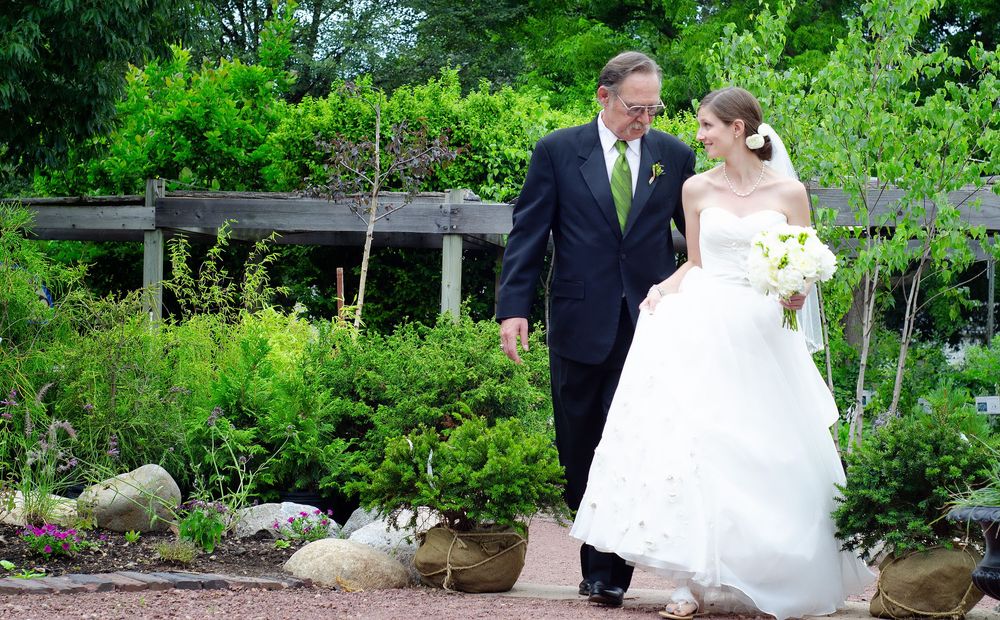 A Colorado couple in wedding attire poses for photos in a lush garden setting with stone landscaping and greenery.