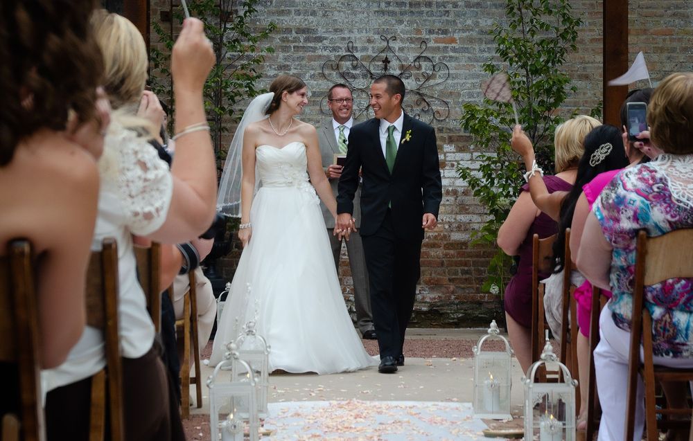 Denver Wedding ceremony guests line the brick courtyard walkway throwing rose petals as newlyweds walk down the aisle.