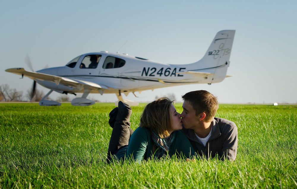 A small private aircraft parked on a grassy airfield with rolling green hills in the background.