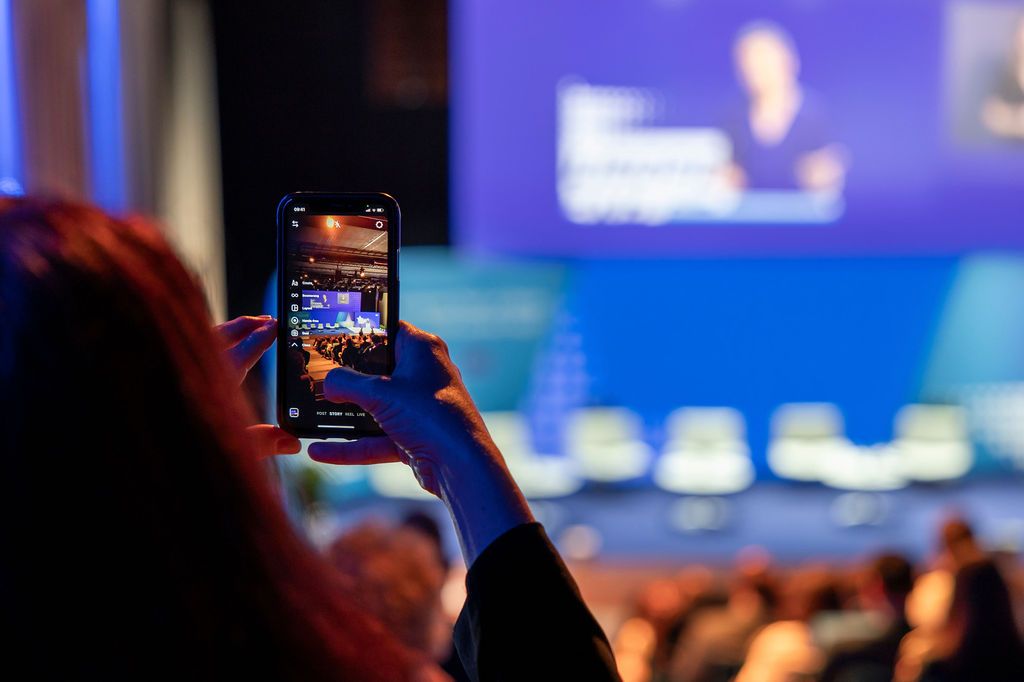Audience members watching a presentation in a darkened conference room with blue lighting.