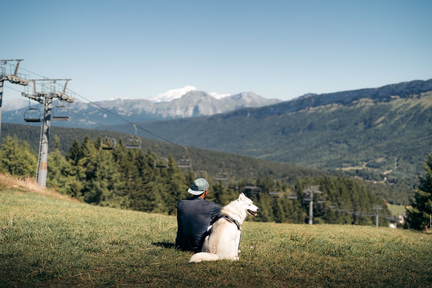 Un promeneur et son chien regardent le massif des abuges et le mont-blanc en arrière plan depuis le télésiège de l'orionde à la Féclaz
