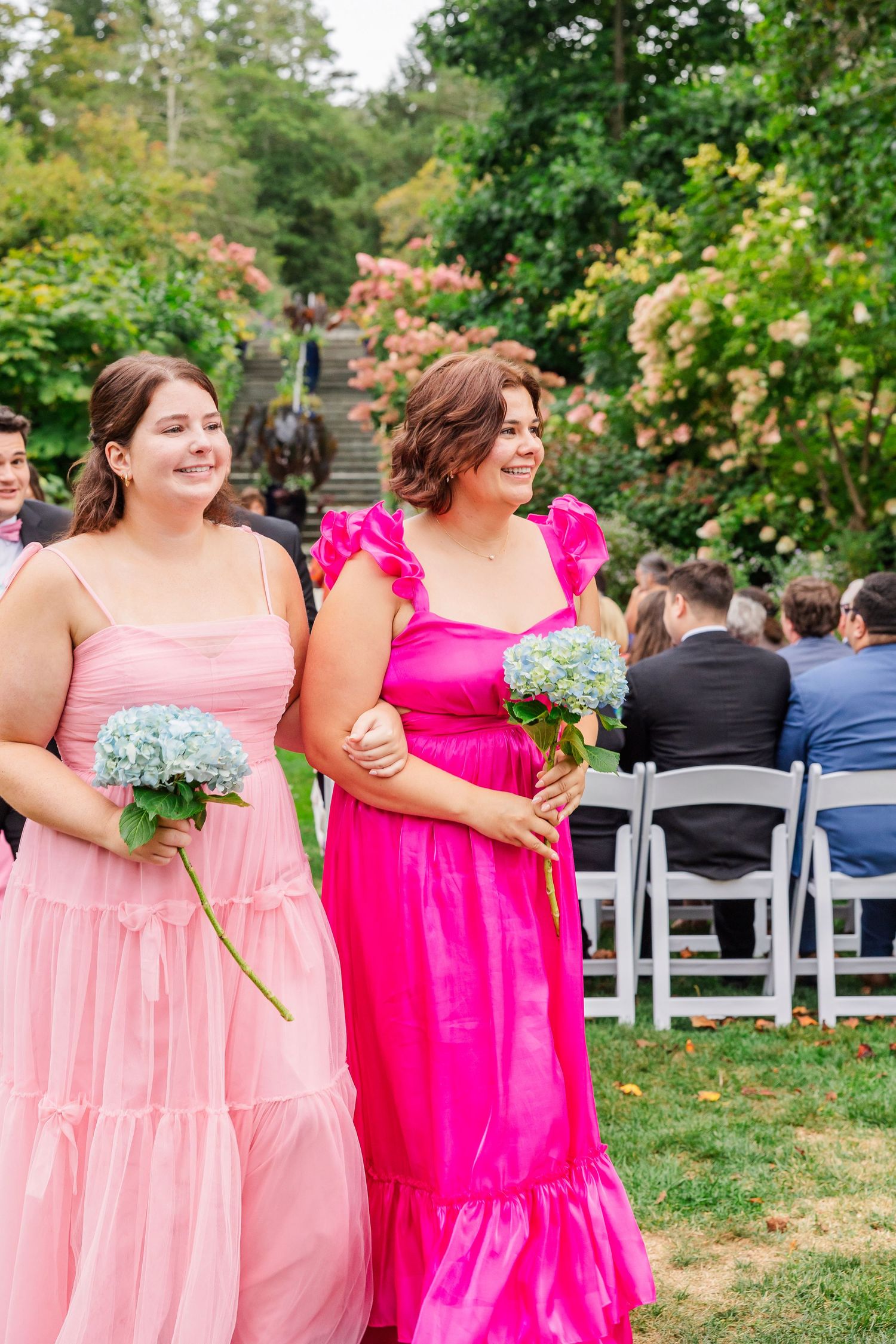 Bridesmaids in pink and hot pink dresses stand together at an outdoor garden wedding ceremony.