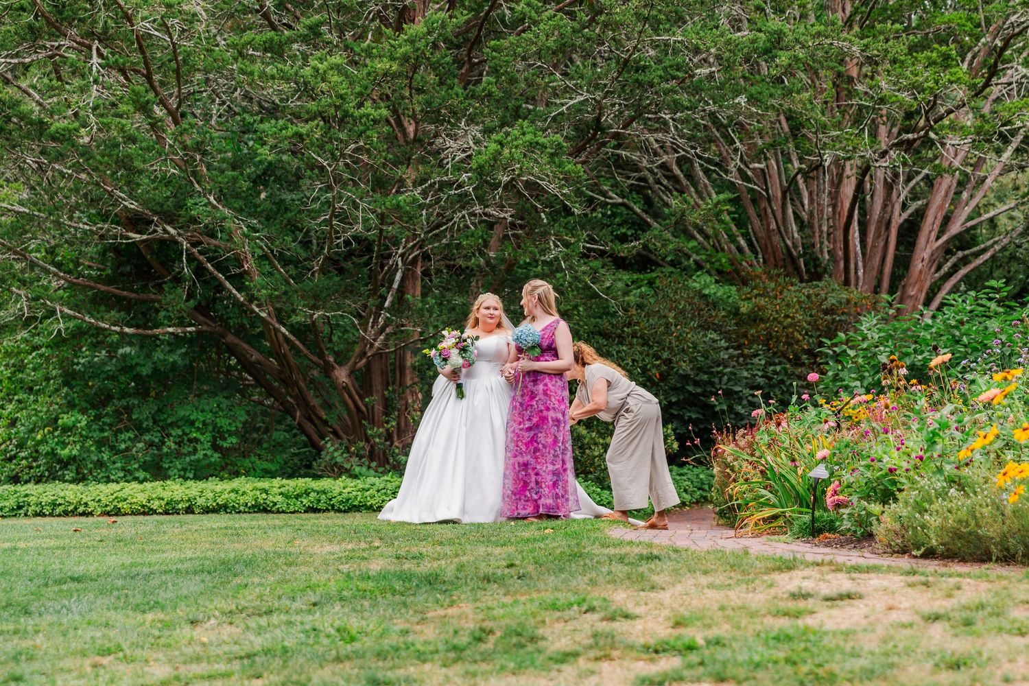 Wedding party poses in a lush garden setting with vibrant summer flowers and greenery.