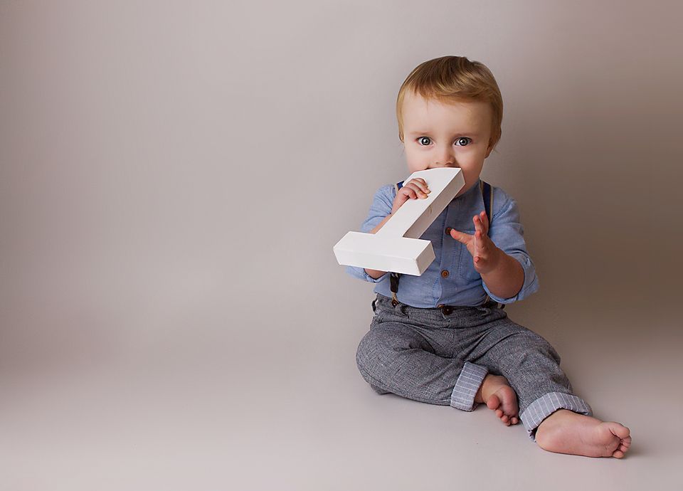 A small child in gray clothing sits and plays while moving through different poses on a light colored backdrop.
