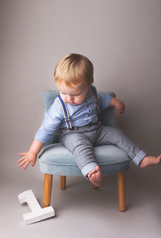 A toddler in gray overalls balances playfully across a light blue cushioned ottoman in a series of progressive movements.