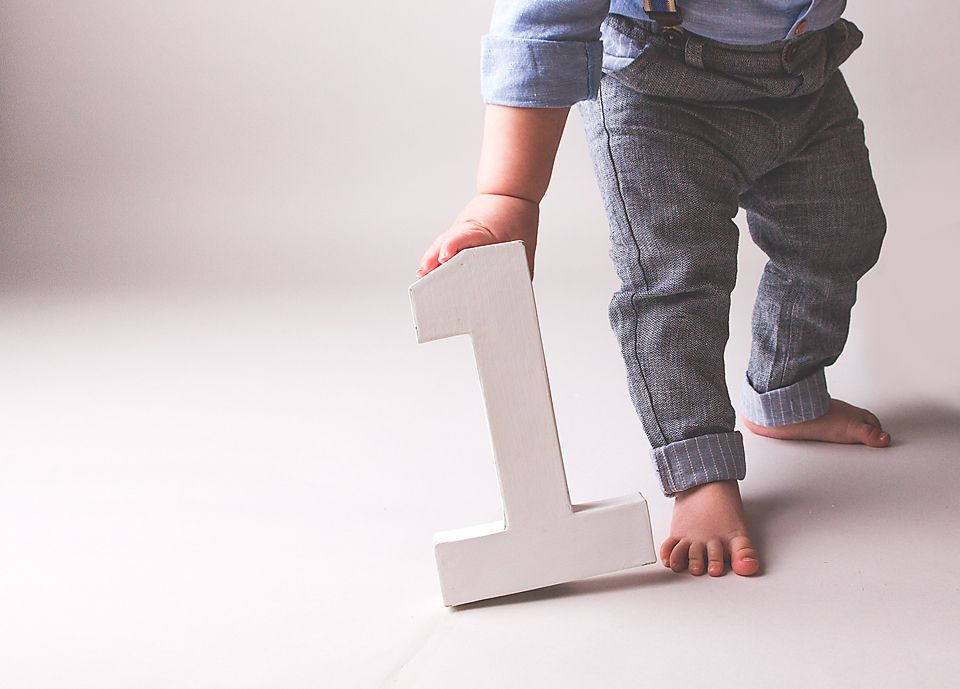 Small feet in denim jeans take first steps while holding onto a white letter A for support.