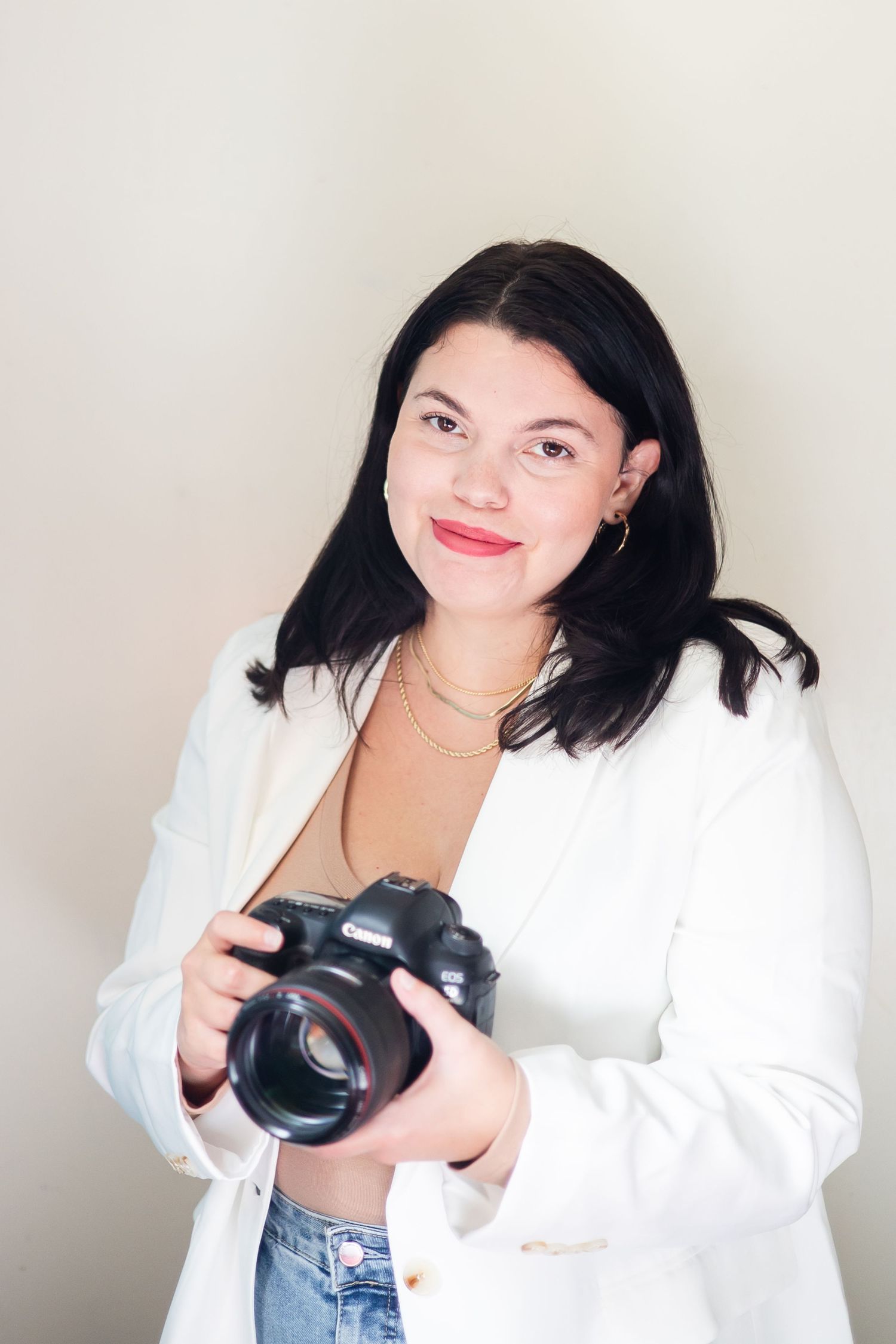 Professional photographer in WV white blazer and jeans holding camera equipment in creative studio setting.