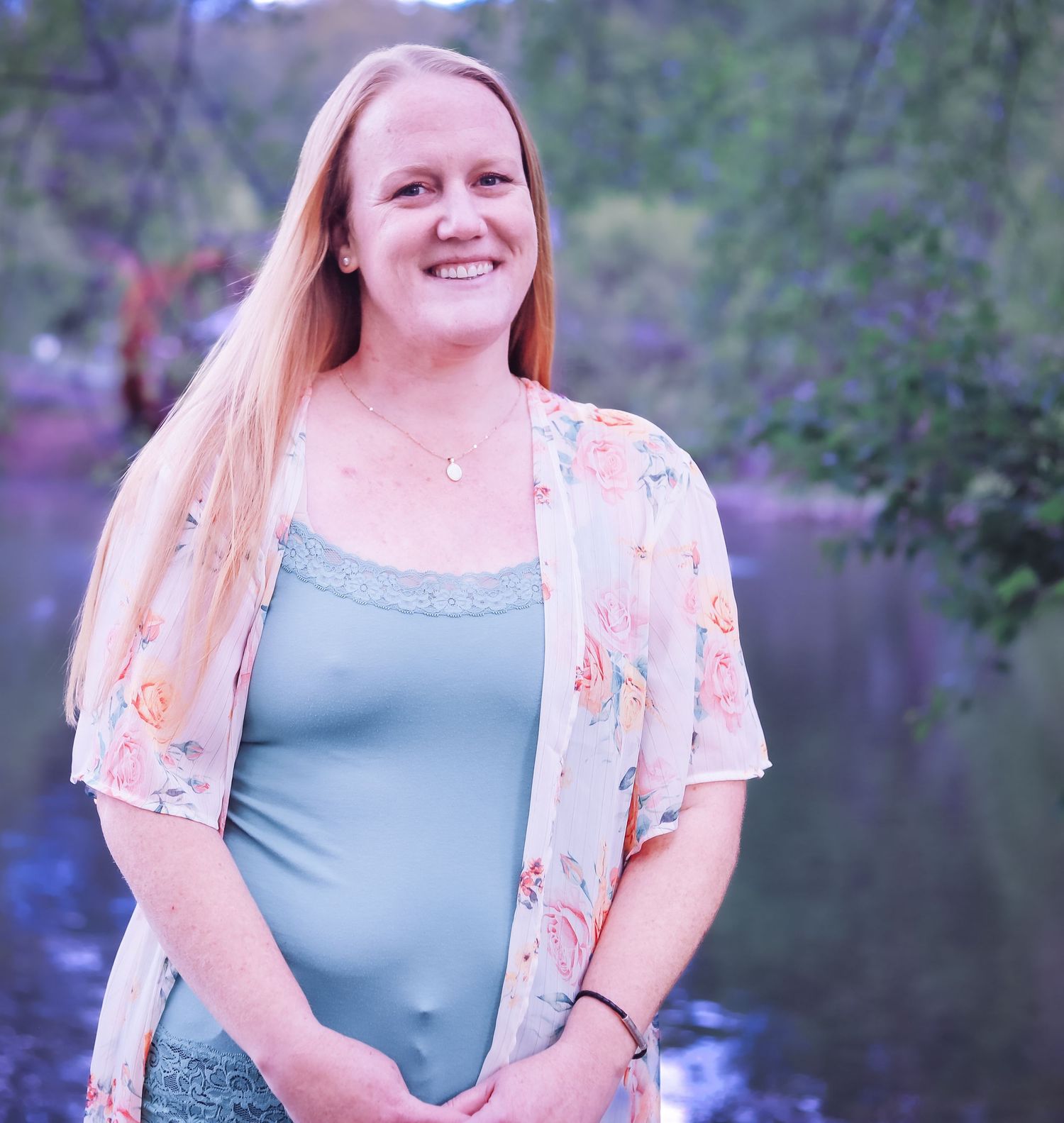A person in a light blue top and peach lace cardigan poses outdoors against a blurred natural background.