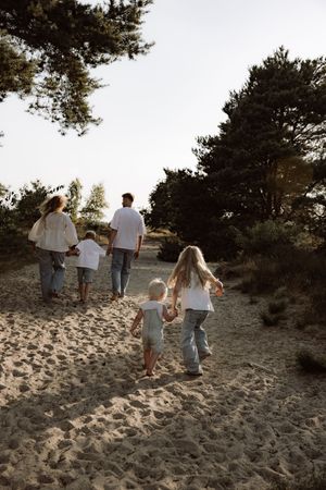 Family walking up sandy hill together during sunset photoshoot.