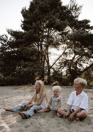 Family lying together on sandy beach near pine trees at sunset.