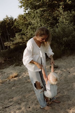 Adult and child playing together on sandy ground surrounded by trees and greenery.