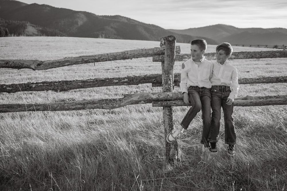 Black and white photo of children leaning against wooden fence posts in mountain field.