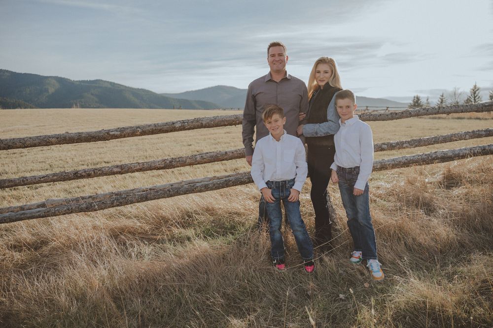 Family standing together by rustic fence in mountain field during golden hour.