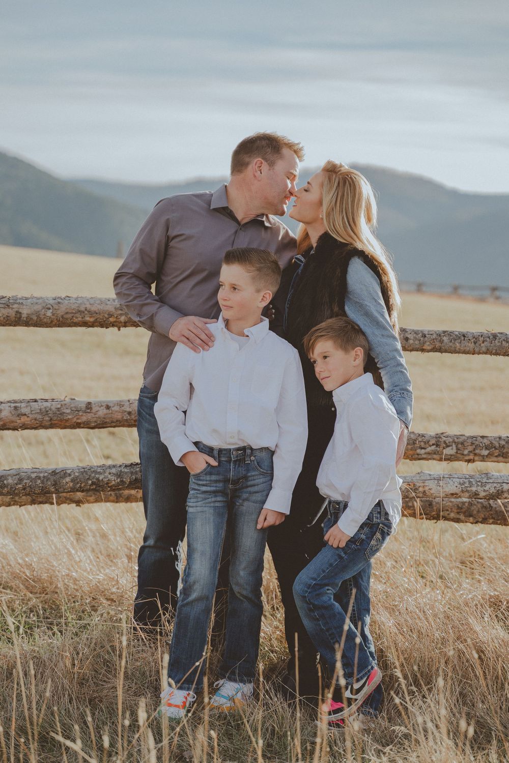 Intimate family portrait by rustic fence with rolling hills and mountains in background.