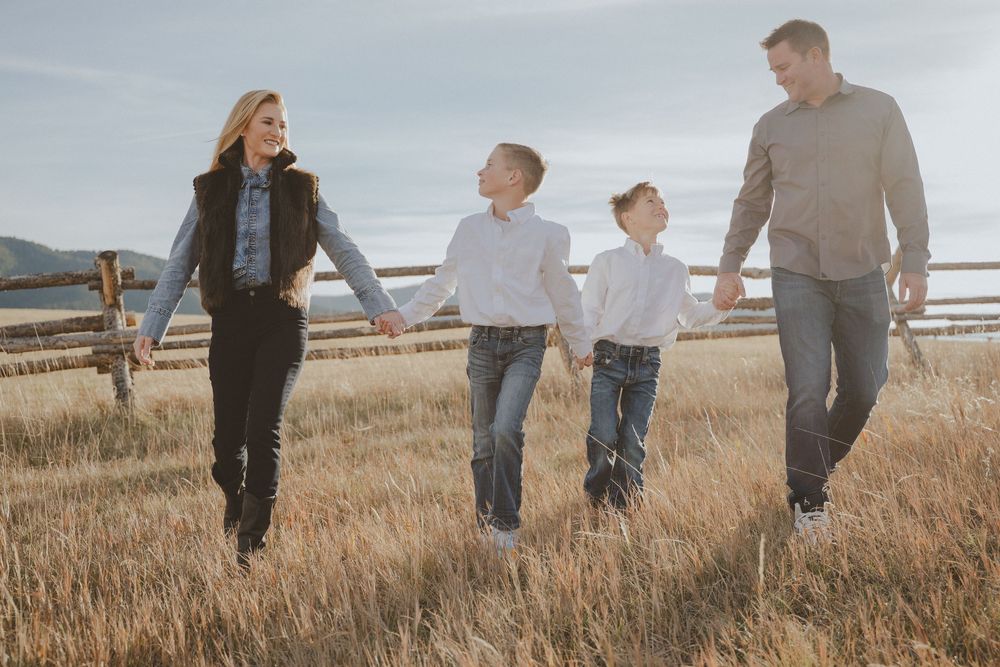 Family walking together through golden grass field with mountain backdrop.