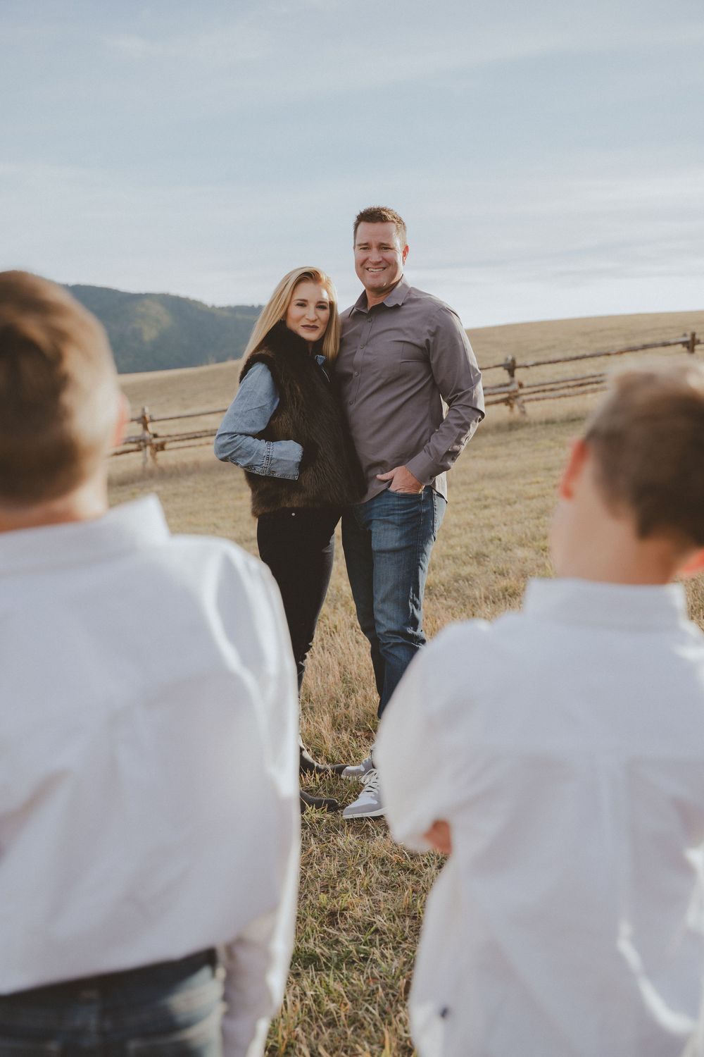Family photoshoot in a rustic field setting with mountains and cloudy sky.