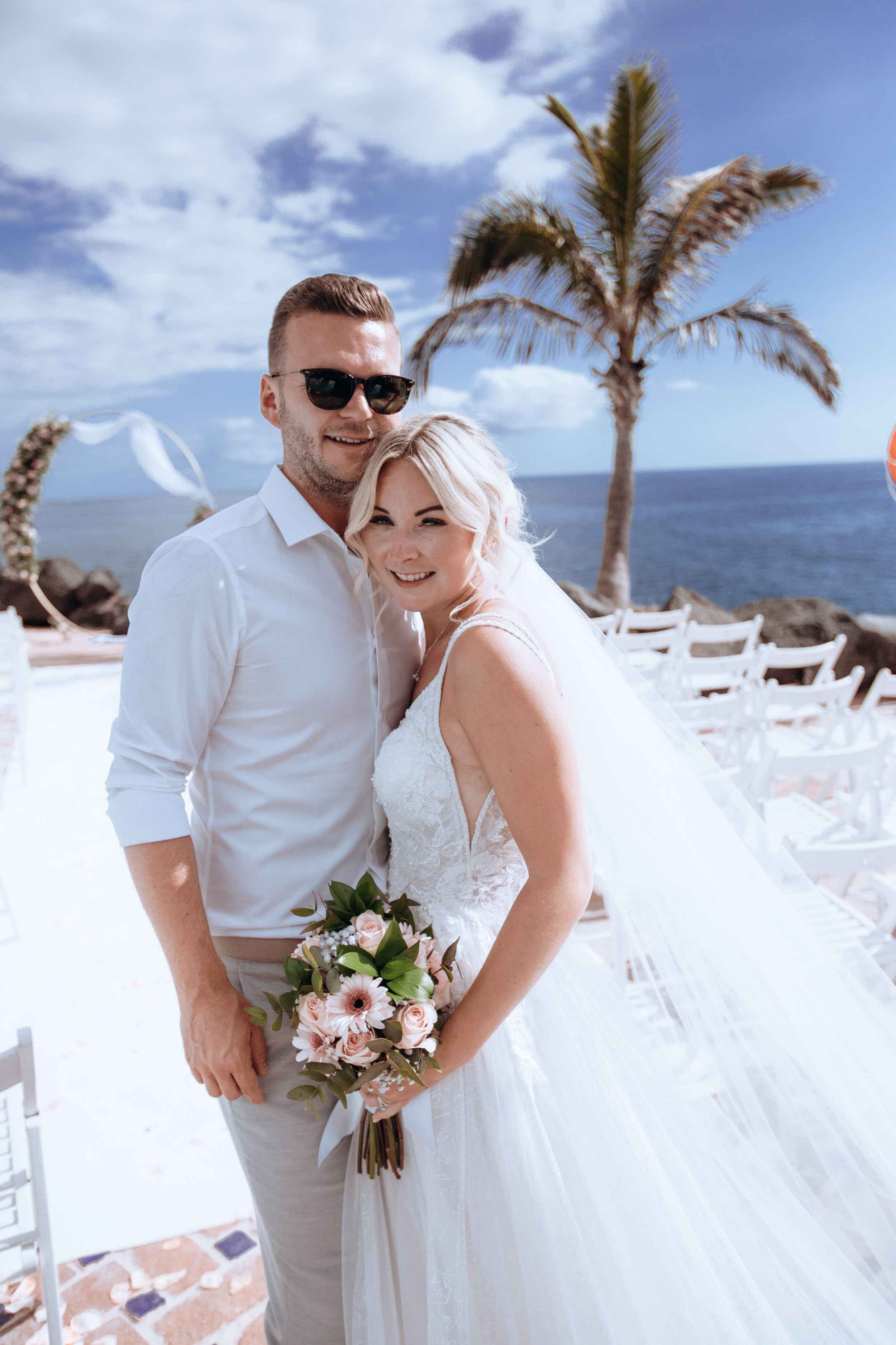 Wedding couple shares intimate moments at tropical beach venue with palm trees.