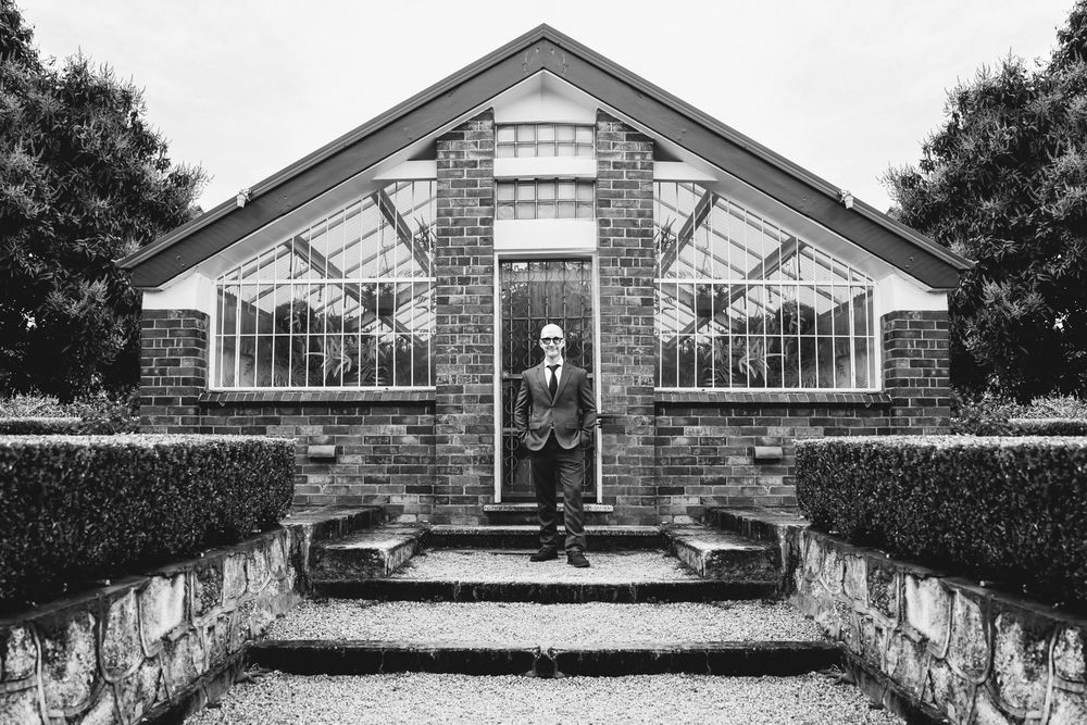 A black and white panoramic collage shows a historic brick entrance with decorative iron gates and stone steps.