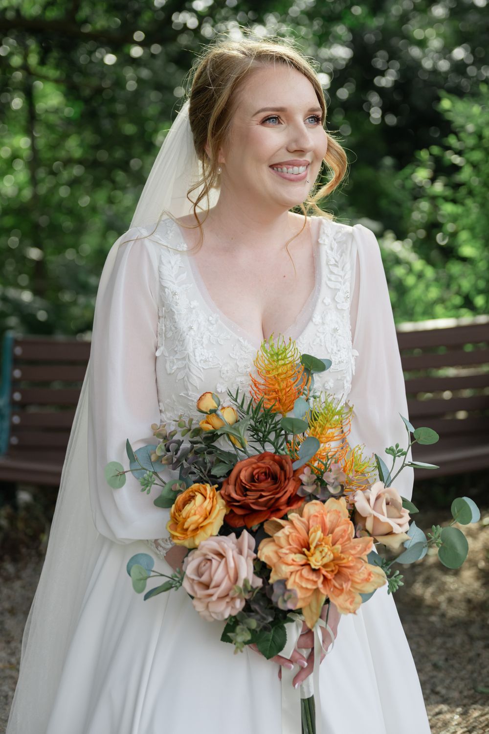 A stunning bridal portrait featuring a white lace wedding dress and vibrant autumn-toned bouquet with roses and dahlias.
