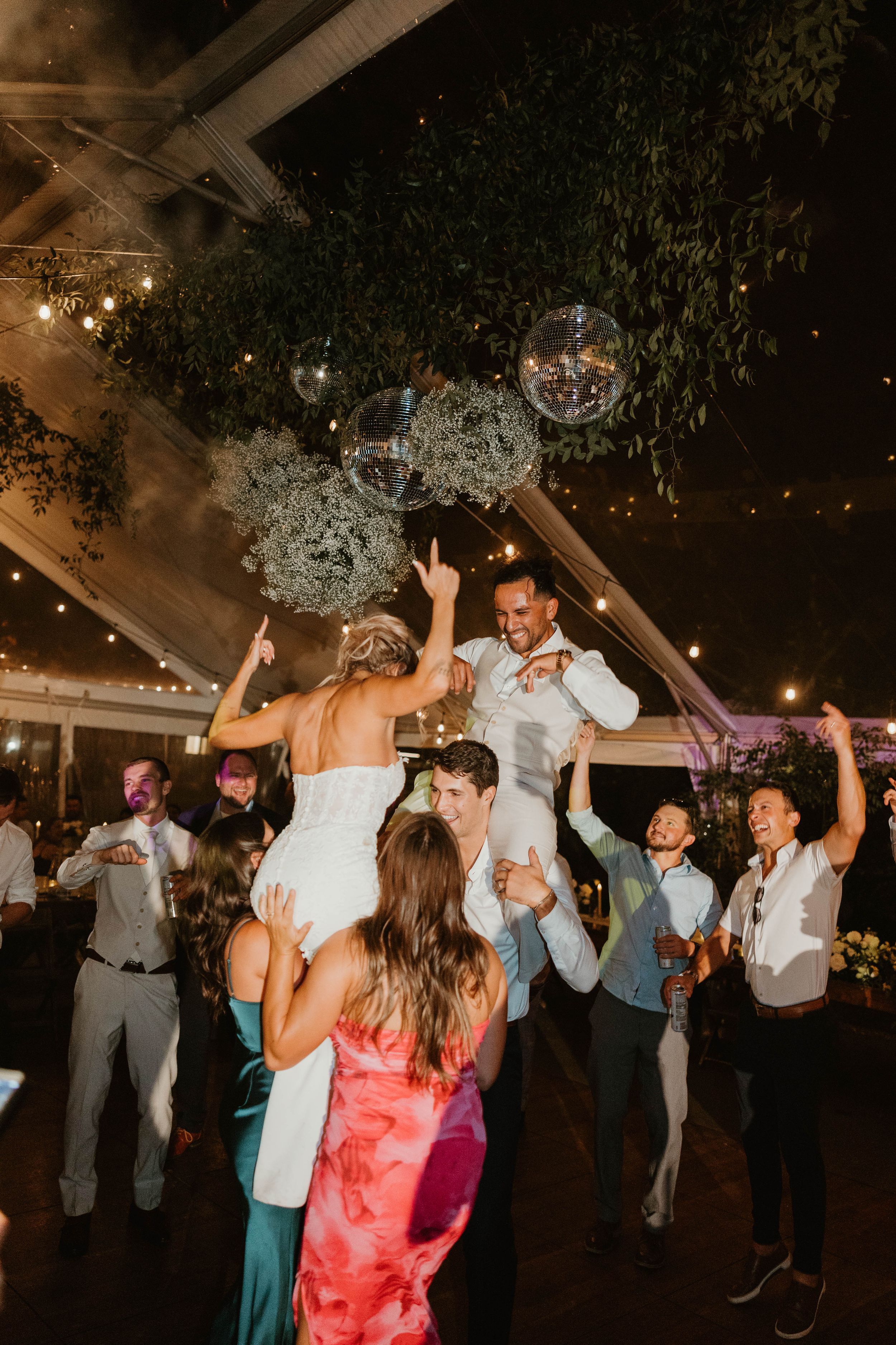 Wedding reception dance party with guests celebrating under twinkling lights.