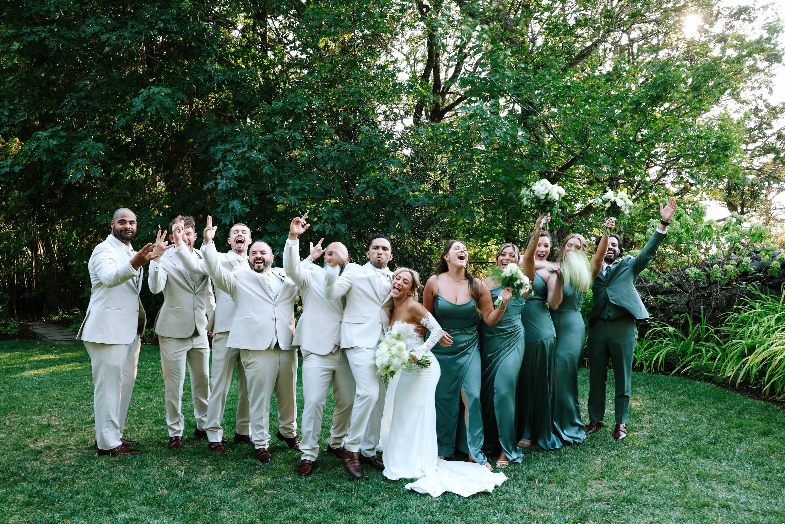 Wedding party group photo on green lawn with coordinated white and sage green attire.