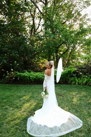 Wedding dress train spread beautifully across green lawn in outdoor garden setting.