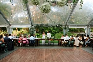 Clear-top tent wedding reception with elegant table settings and floral decorations.