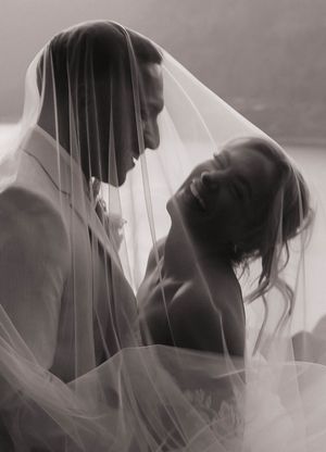Intimate black and white portrait of newlyweds sharing a moment under a flowing veil.