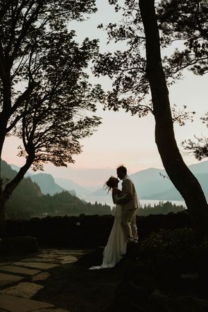 Silhouetted couple shares an intimate moment at sunset with mountain and lake views in the background.