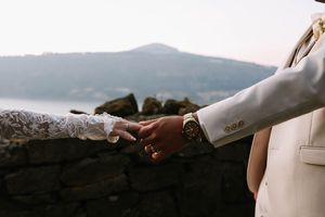 Two people hold hands with mountains and lake in the background at sunset.