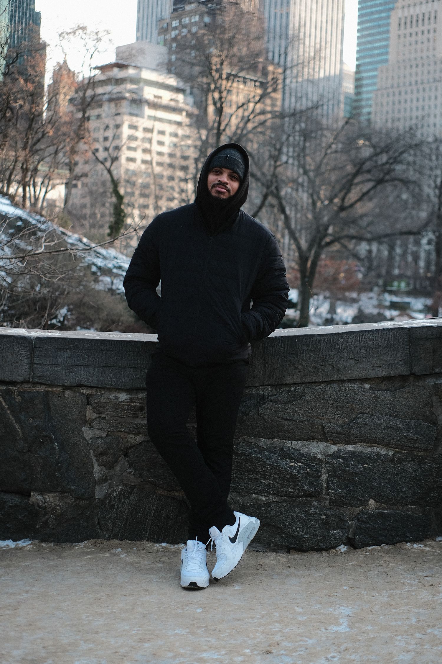 Person in black clothing sitting on stone wall with city skyscrapers in background.