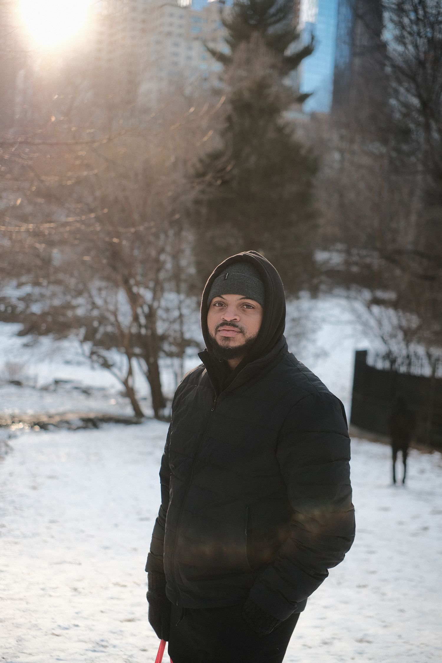 Person in black winter coat and beanie standing in snowy park.