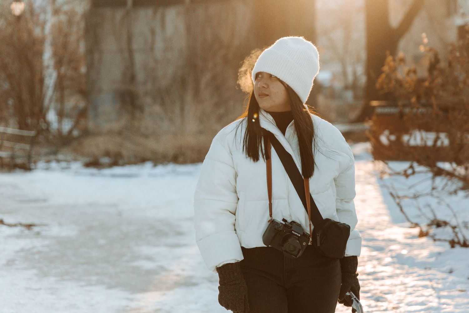 Person in winter attire walking through snowy landscape at sunset.