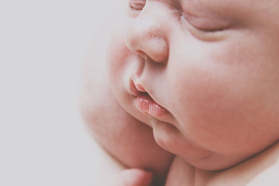 Close-up portrait of a sleeping newborn baby with soft pink tones and delicate features.