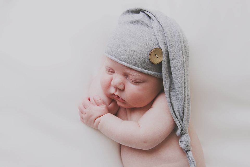 Peaceful sleeping newborn wearing a grey knit cap against a light background.