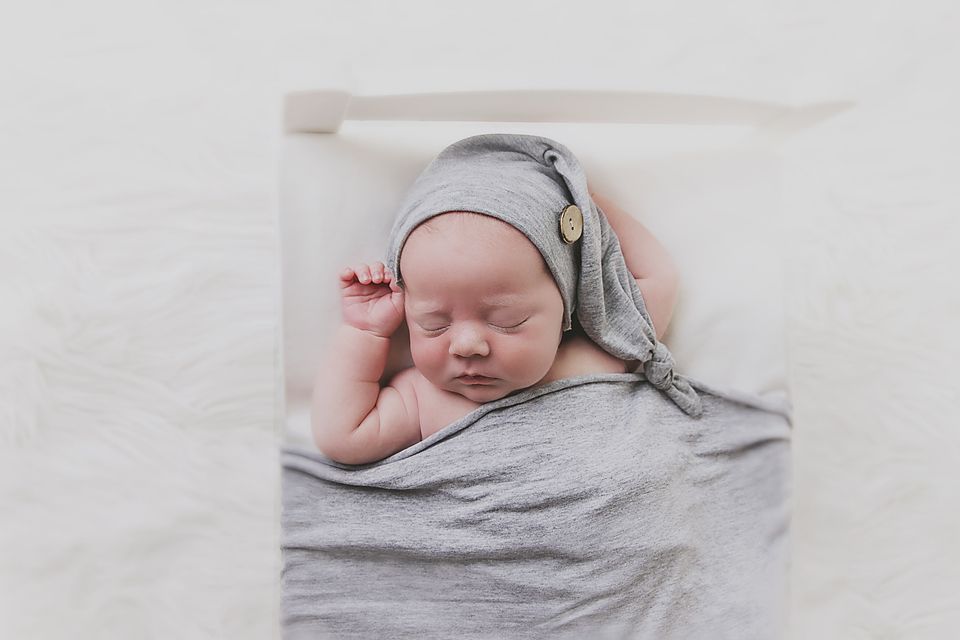 Sleeping newborn wrapped in soft grey blanket during professional photoshoot.