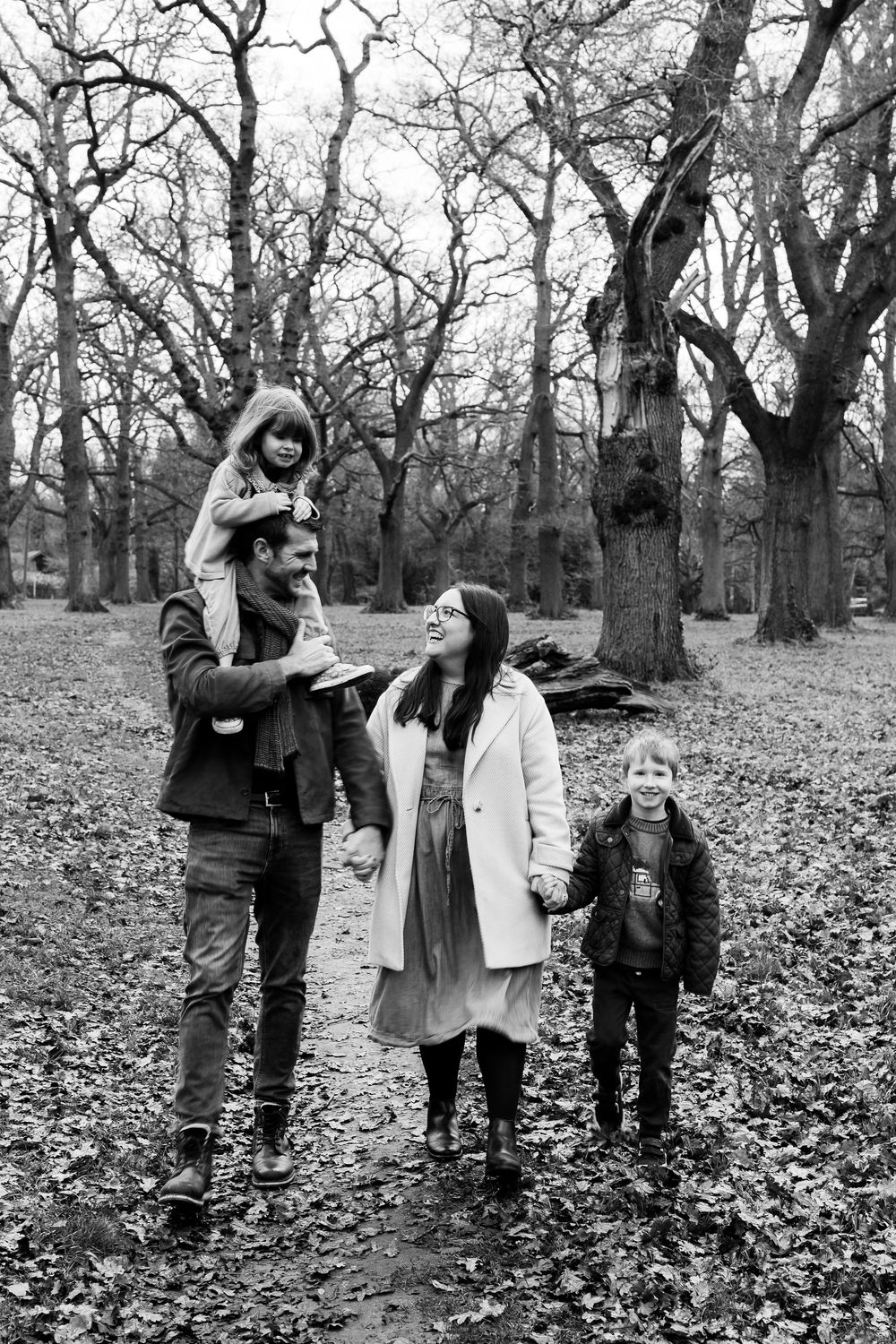 A group of people playfully interacting in a wooded area covered with fallen autumn leaves.