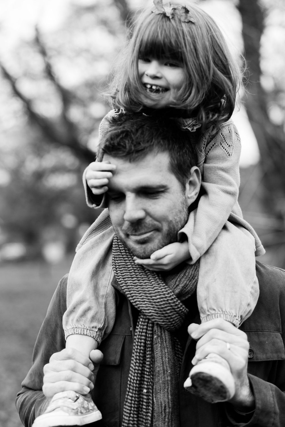 Black and white photo series showing playful parent-child interaction with a knit scarf and winter clothing outdoors.