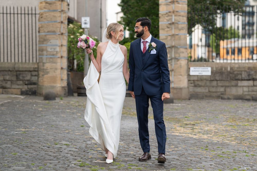 A couple walks together on cobblestone path during their wedding day.