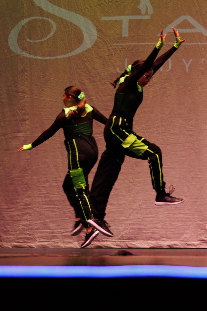 Sequence of dance movements showing a performer in neon yellow attire leaping and spinning against a reddish backdrop.