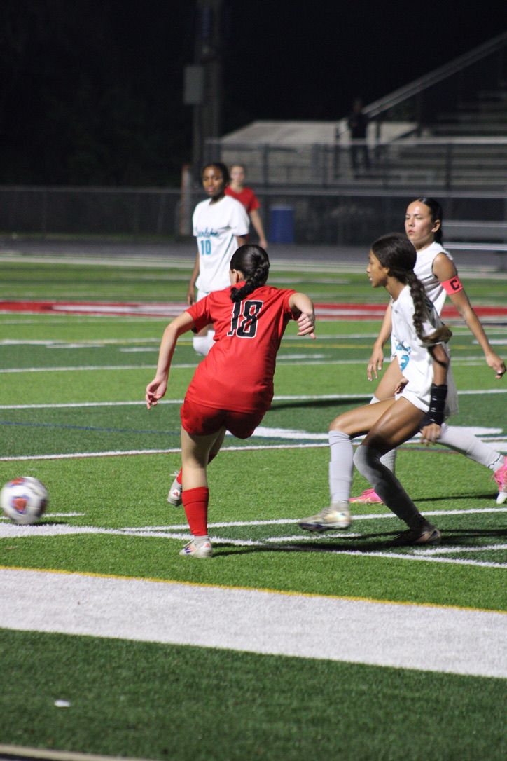 Soccer players compete for the ball during a nighttime match on an artificial turf field.