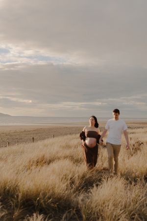 A couple stands together in a golden wheat field at sunset with mountains in the distance.