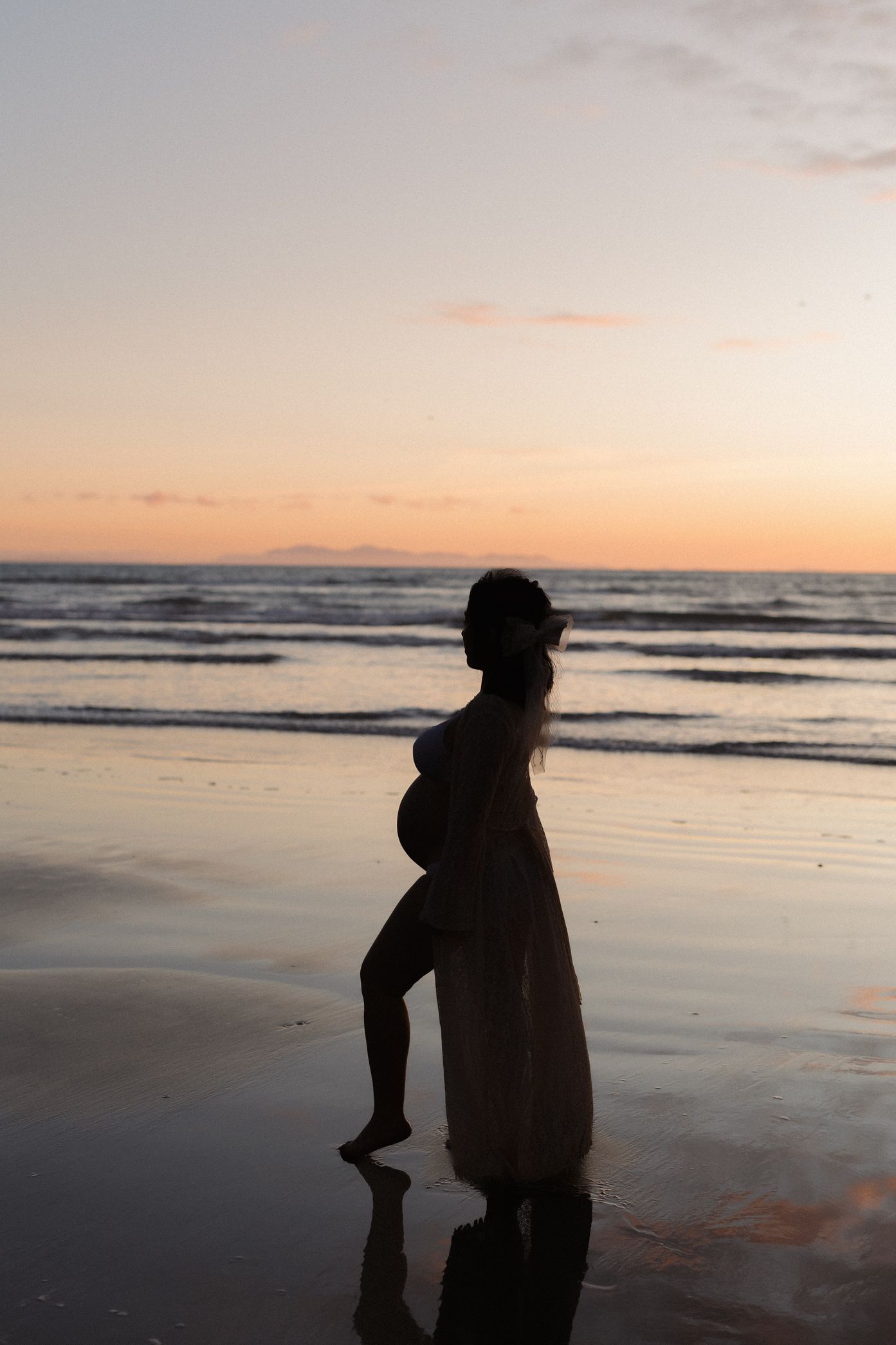 Silhouettes of two people walking along a beach at sunset with ocean waves and warm orange sky in the background.