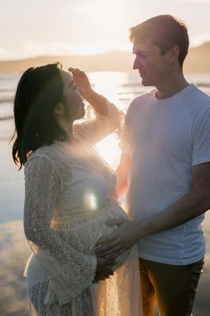 A couple embraces on the beach during golden hour as sunlight creates a warm romantic glow around them.