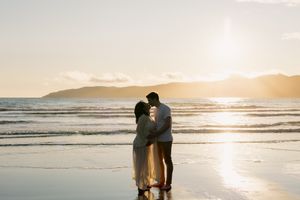 Silhouetted couple walking together on a beach at sunset with waves rolling onto shore in golden light.