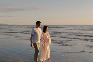 A couple walks hand in hand along a serene beach at sunset, creating silhouettes against the ocean waves.
