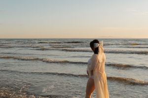 A person walks along a sandy beach at sunset while waves roll onto the shore.