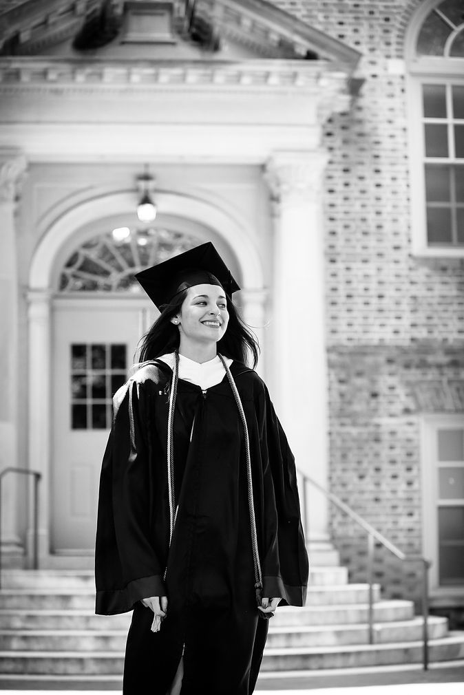 Graduate in cap and gown smiling outside classic brick university building.